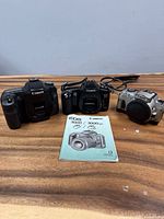 Three Canon camera bodies and one manual displayed on tabletop