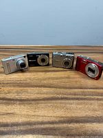 Front view of four compact cameras: Kodak black, Casio silver, Nikon Coolpix silver, Panasonic Lumix red
