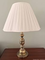 Full view of brass table lamp with pleated shade on wooden surface