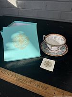teacup, saucer, box and info card displayed with ruler