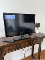 Front view of LG TV on stand with remote visible