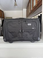 Front view of large Tumi suitcase showing dual zip pockets and logo plaque