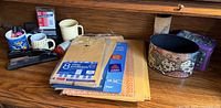 All office supplies on wooden desk including envelopes, stapler, mugs with pens, tins
