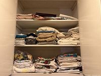 Open linen closet with folded towels, sheets, tablecloths, napkins and bag of curtain rings