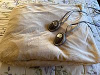 Beige heated blanket folded on bed with two digital controllers visible
