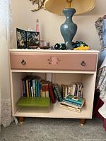 Front view of cream-painted cabinet with pink floral drawer and open shelf