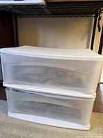 Two stacked white plastic Sterilite under-bed drawers with visible contents inside