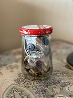 Full view of glass jar with red lid filled with assorted buttons