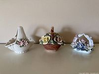 Three porcelain flower basket figurines displayed side by side