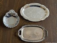 Three small silver-tone metal trays displayed on wooden surface