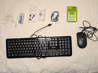 Entire lot laid out: keyboard, mouse, calculator, three earbud sets, LED string lights with battery pack