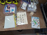 Overall view of craft items on workbench including finger knitting kit, tie-dye organizer, stencils pouch, jar of rocks, spool of twine, patch sheet
