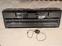 Rear view of Casio LK-190 keyboard with attached power adapter and removed back panel