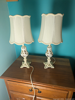 Front view of both matching cream and gold table lamps on wooden surface