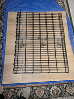 Folded black metal pen resting on vinyl tile floor mat over blue tarp