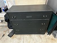 Front view of matte black dresser with carved trim and metal pulls