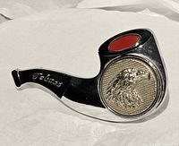 Overall view of chrome pipe-shaped belt buckle showing red enamel accent, spinning eagle medallion and script logo