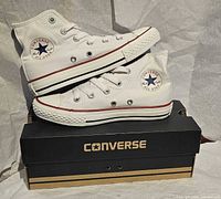 side view of both white high-top sneakers stacked on branded shoebox