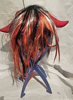 Rear view of long red and black wig with devil horns on a stand