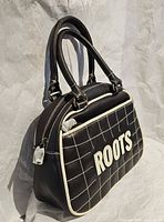Side angle of black quilted Roots handbag with white piping and dual handles