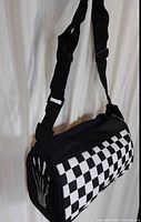Overall view of black and white checkerboard shoulder bag hanging, showing strap and main pattern