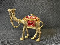 Full side view of gold-tone enameled camel trinket box standing on fabric backdrop