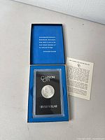 Blue presentation box open showing plastic holder with coin and pamphlet