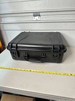 Closed black hard case on table with tape measure showing length