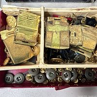 Open box showing brass belt buckles, loose brass and grey buttons