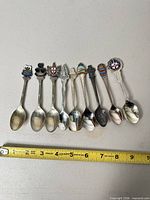 All eight souvenir spoons lined up with ruler showing 4–5 in length