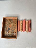 Five wrapped rolls of wheat pennies beside wooden tray of loose coins