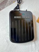 Closed George Foreman grill showing brand on lid and power cord