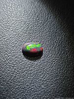 Loose oval black opal showing green and red fire on textured background