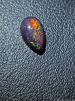 Pear cabochon opal showing multicolored flashes on black background