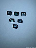six loose emerald-cut sapphires grouped on white background