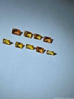 Nine baguette-cut yellow and orange sapphires on white background