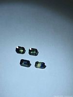 Four emerald-cut bi-colored sapphires on neutral background
