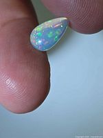 Pear cabochon opal on fingertip showing play-of-color