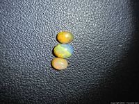 Three oval chocolate opal cabochons aligned vertically on textured black surface