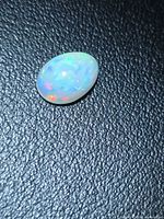 Pear cabochon Ethiopian opal on textured background showing multi-color flashes