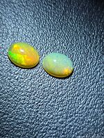 Two oval cabochon opals showing green and orange flashes on black textured background