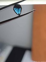 pear-cut deep blue spinel held by tweezers, face-up view