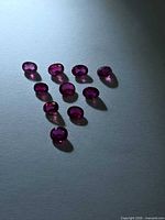 Ten small oval rubies arranged in triangle formation on neutral background