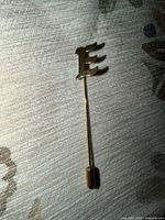 Full view of gold-tone stick pin showing letter E finial and clutch cap