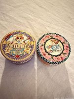 Two Mary Engelbreit round trinket boxes side by side showing top artwork