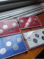 Four coin sets in plastic holders on wooden surface