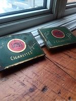 Both Lucky Strike tins on wooden floor showing size and color