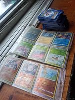 Binder sleeve page displaying nine Pokémon cards including holographic and full-art varieties next to loose stack