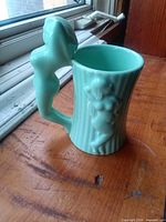 Right side view of turquoise ceramic mug with nude figure handle and bas-relief