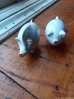 Front view of both white ceramic pig shakers on wooden surface